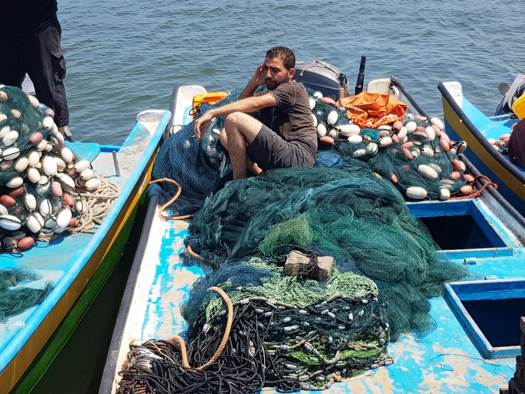 صياد غزي يجلس فوق شباك الصيد